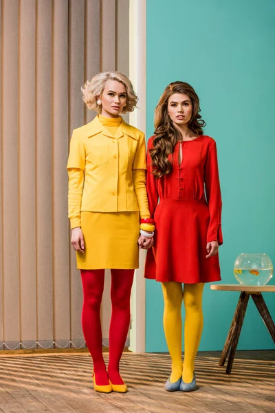 Mujeres en brillante ropa de estilo retro tomados de la mano en el apartamento colorido, concepto de casa de muñecas - foto de stock