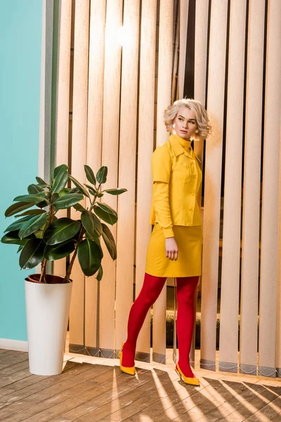 Стомлена ретро-стилізована жінка, що стоїть на рослині фікус у вазоні в барвистій квартирі, концепція лялькового будинку — стокове фото