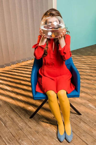 Затемнений вид жінки з золотою рибою в акваріумі, що сидить на стільці в барвистій квартирі, концепція лялькового будинку — стокове фото