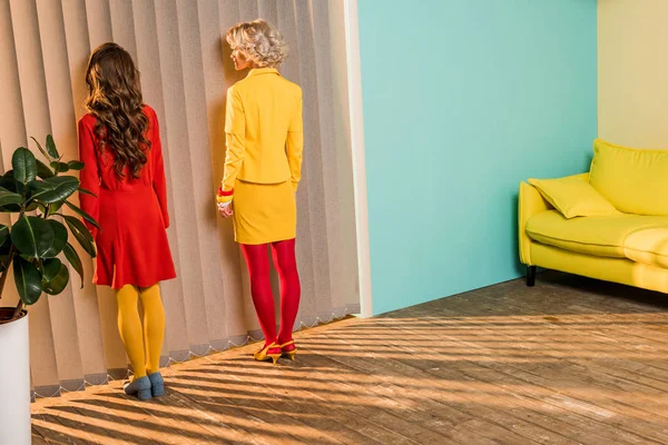 Rückansicht von Frauen in heller Kleidung, die am Fenster vor der bunten Wohnung stehen, Puppenhauskonzept — Stockfoto