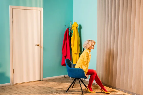 Vista lateral de la mujer de estilo retro pensativo sentado en la silla en el apartamento luminoso, concepto de casa de muñecas - foto de stock