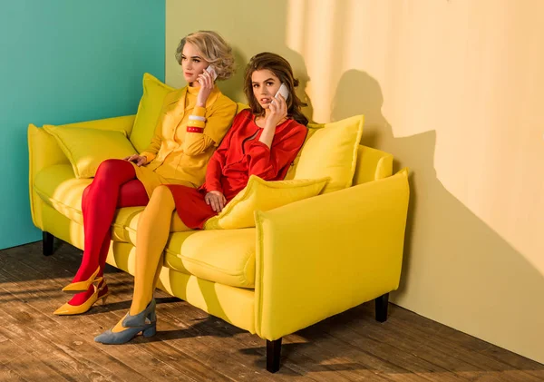 Жінки в стилі ретро розмовляють на смартфонах на жовтому дивані, концепція лялькового будинку — стокове фото