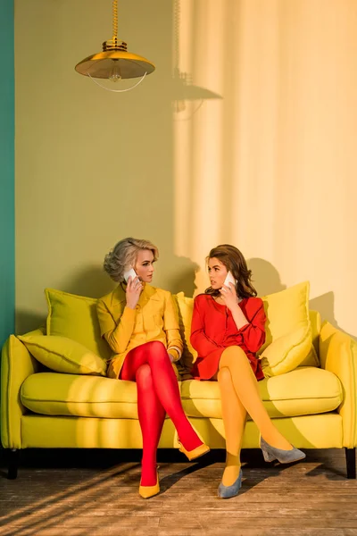 Mujeres de estilo retro hablando en teléfonos inteligentes en sofá amarillo, concepto de casa de muñecas - foto de stock