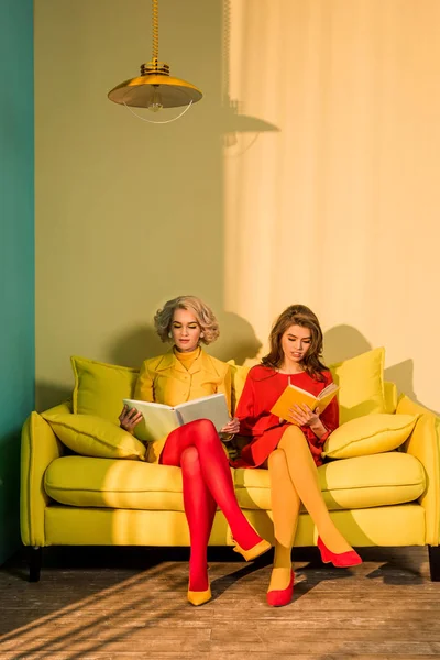 Femmes dans des vêtements rétro lecture de livres assis sur un canapé jaune à appartement lumineux, concept de maison de poupée — Photo de stock