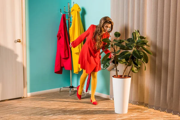 Fille à l'ancienne en robe rouge arrosage plante avec arrosoir à la maison — Photo de stock