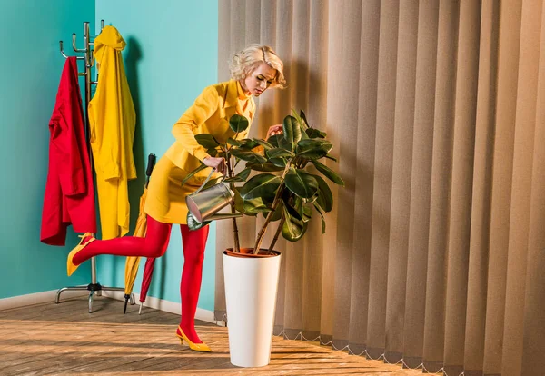 Élégant attrayant femme en robe colorée arrosage plante avec arrosoir à la maison — Photo de stock