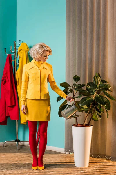 Retro styled beautiful woman in colorful dress watering plant with watering can at home — Stock Photo