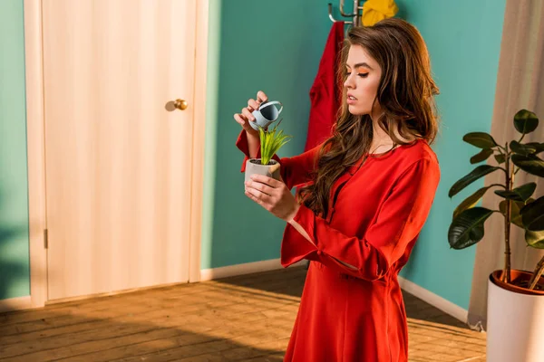 Side view of old-fashioned woman in red dress watering potted plant with small watering can at home — Stock Photo