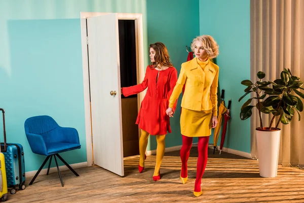 Красиві дівчата в стилі ретро в барвистих сукнях, що входять в квартиру і тримаються за руки вдома — стокове фото