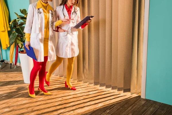 Image recadrée de médecins de style rétro en collants colorés pointant sur le presse-papiers en clinique — Photo de stock