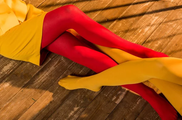 Imagen recortada de las niñas en medias de colores y vestidos sentados en el suelo en casa - foto de stock