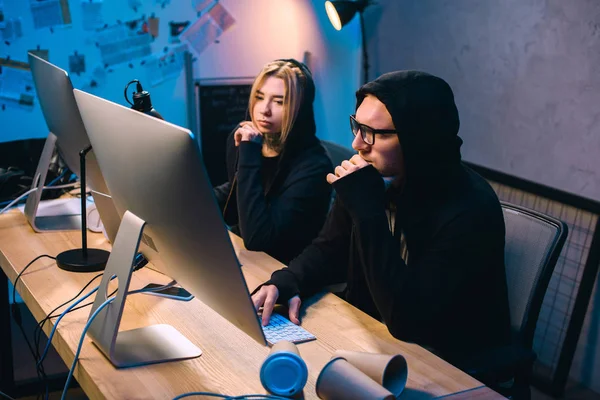 Pareja de jóvenes hackers trabajando juntos en la habitación oscura - foto de stock