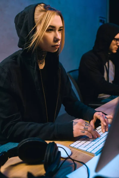 Hacker femelle travaillant sur de nouveaux logiciels malveillants avec complice dans la chambre noire — Photo de stock