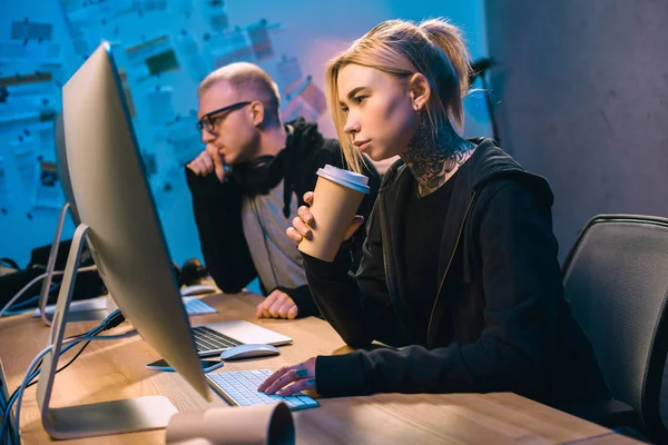 Junge Hackerin trinkt Kaffee und arbeitet mit Komplizin an Malware — Stockfoto