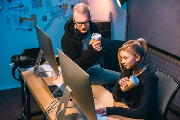 Couple of hackers drinking coffee to go and working on malware in dark room — Stock Photo