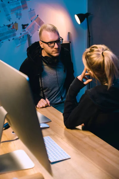 Pareja de hackers hablando entre sí en el lugar de trabajo en la habitación oscura - foto de stock