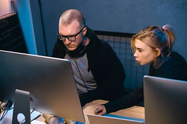 Jeune couple de pirates qui regardent l'écran d'ordinateur ensemble sur le lieu de travail — Photo de stock