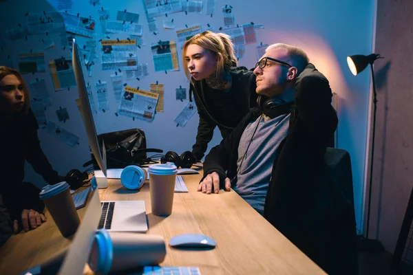 Pareja de hackers mirando la pantalla de la computadora juntos en la habitación oscura - foto de stock