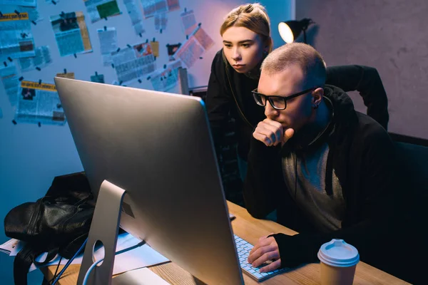 Casal sério de hackers trabalhando com computador juntos no quarto escuro — Fotografia de Stock