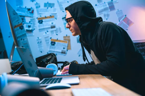 Serious hooded hacker working with computer to develop malware — Stock Photo