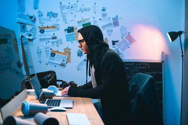 Seitenansicht eines vermummten jungen Hackers, der mit dem Computer arbeitet — Stockfoto