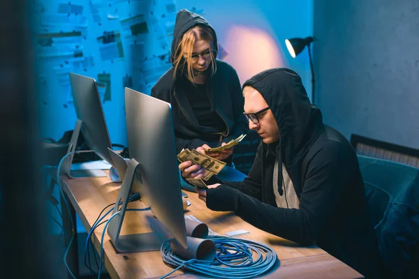 Couple of hackers counting stolen cash in dark room — Stock Photo