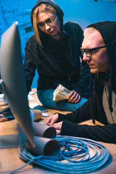Pareja de hackers con pila de dinero en efectivo en el lugar de trabajo - foto de stock
