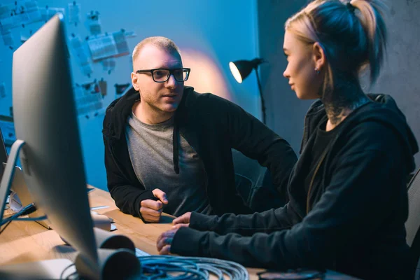 Couple of hackers chatting at workplace in dark room — Stock Photo