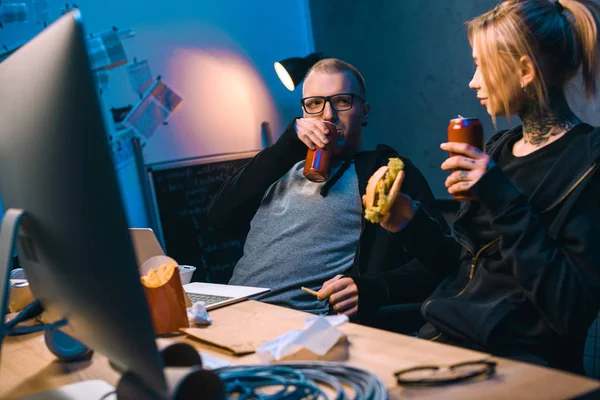 Young hackers drinking beer and eating junk food while working on malware — Stock Photo