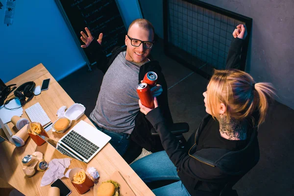 High angle view of celebrating couple of hackers clinking cans of beer at workplace — Stock Photo