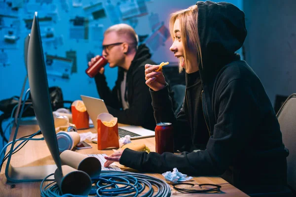 Vue latérale des pirates de manger de la malbouffe tout en travaillant sur les logiciels malveillants — Photo de stock