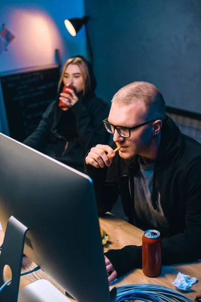 Young hackers drinking beer and eating junk food while working on malware — Stock Photo