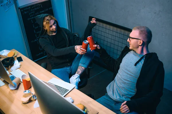 High angle view of couple of hackers clinking cans of beer at workplace — Stock Photo