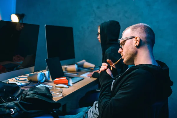 Side view of hacker working on malware with accomplice and smoking — Stock Photo