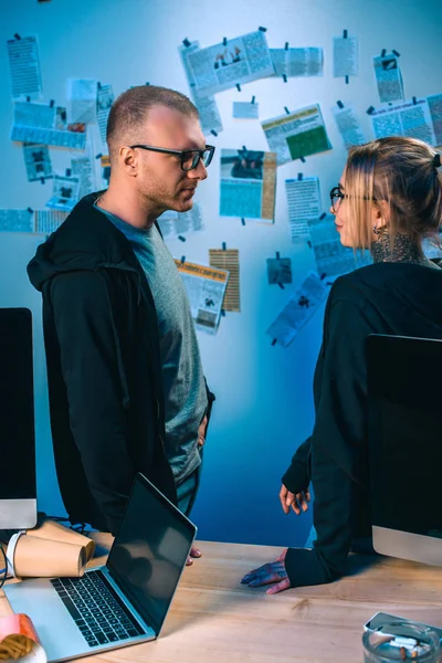 Couple of young hackers standing near desk with computers in dark room — Stock Photo