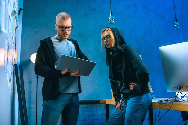 Pareja de hackers con portátil en habitación oscura - foto de stock