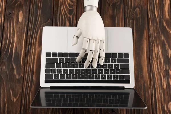 Cropped shot of robot working with laptop on wooden surface — Stock Photo