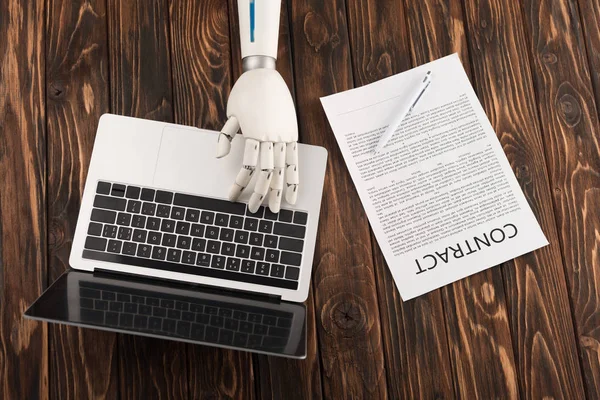 Cropped shot of robot working with laptop on wooden surface with business contract — Stock Photo
