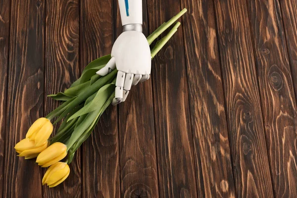 Tiro recortado de robot sosteniendo hermoso ramo de tulipanes amarillos en la superficie de madera - foto de stock