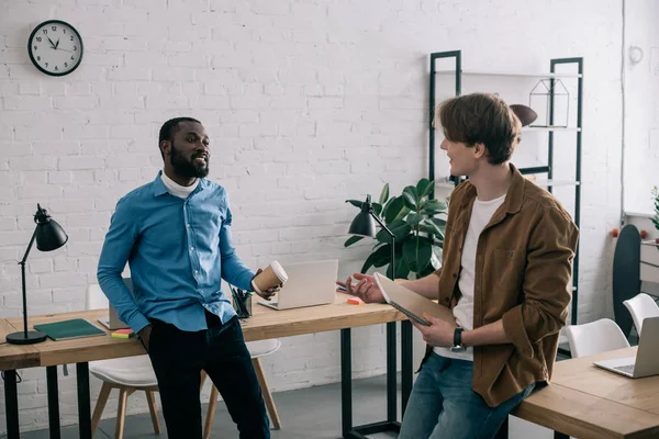 Compañeros de trabajo de negocios multiétnicos con estilo hablando en la oficina moderna - foto de stock