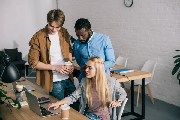 Colegas de negócios multiculturais com copos de café conversando e assistindo no laptop — Fotografia de Stock