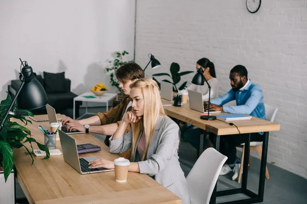 Multicultural business coworkers sitting at table and working on laptops in modern office — Stock Photo