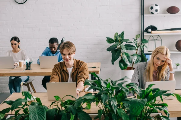 Багатонаціональні бізнес-колеги сидять за столом і працюють на ноутбуках в сучасному офісі — стокове фото