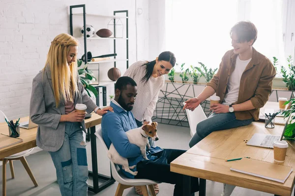 African american businessman sitting with dog surrounded by smiling colleagues — Stock Photo