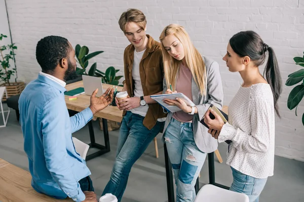 Multiethnic businesspeople with coffee and textbooks having discussion in modern office — Stock Photo