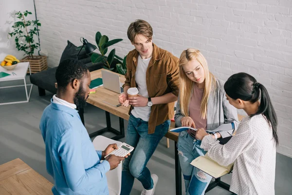 High angle view of multiethnic business colleagues with textbooks, calculator and coffee having meeting — Stock Photo