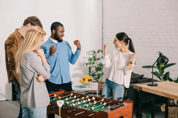 Dos colegas de negocios celebrando la victoria en el futbolín frente a la pérdida de compañeros de trabajo - foto de stock