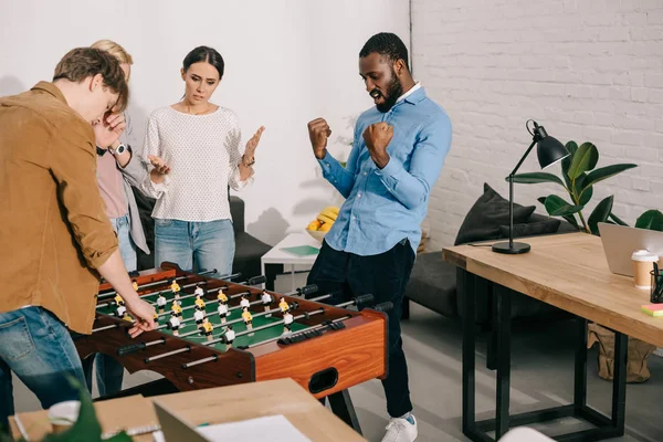 African american celebrating victory in table football and colleagues standing near — Stock Photo