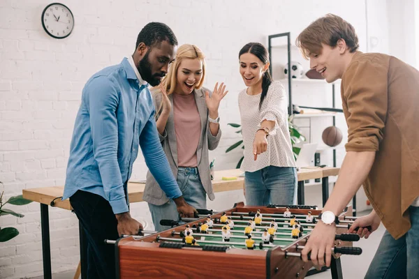 Side view of multicultural businessmen playing table football and female coworker pointing on board game — Stock Photo