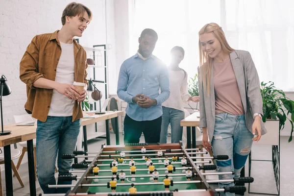 Sonrientes empresarios multiétnicos que van a jugar al futbolín en la oficina moderna - foto de stock